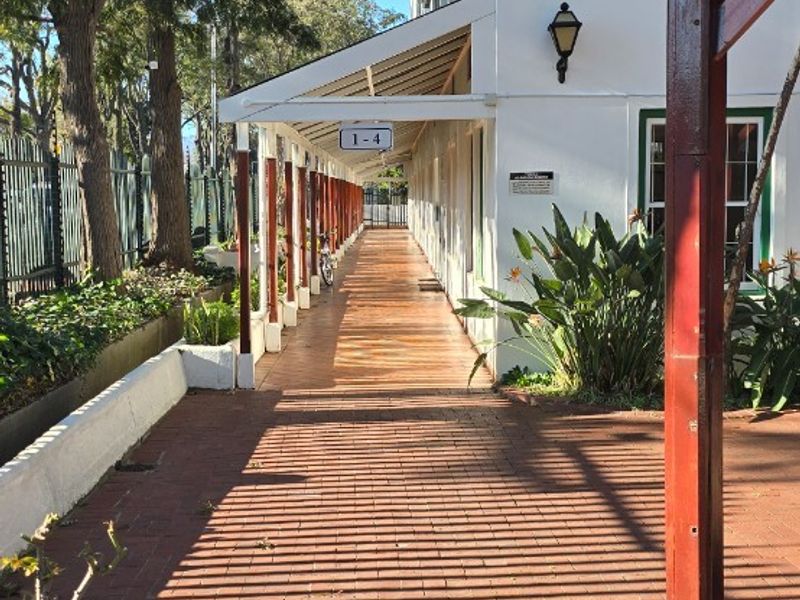 A covered outdoor walkway featuring brick paving and timber support posts, providing access along the side of the building.