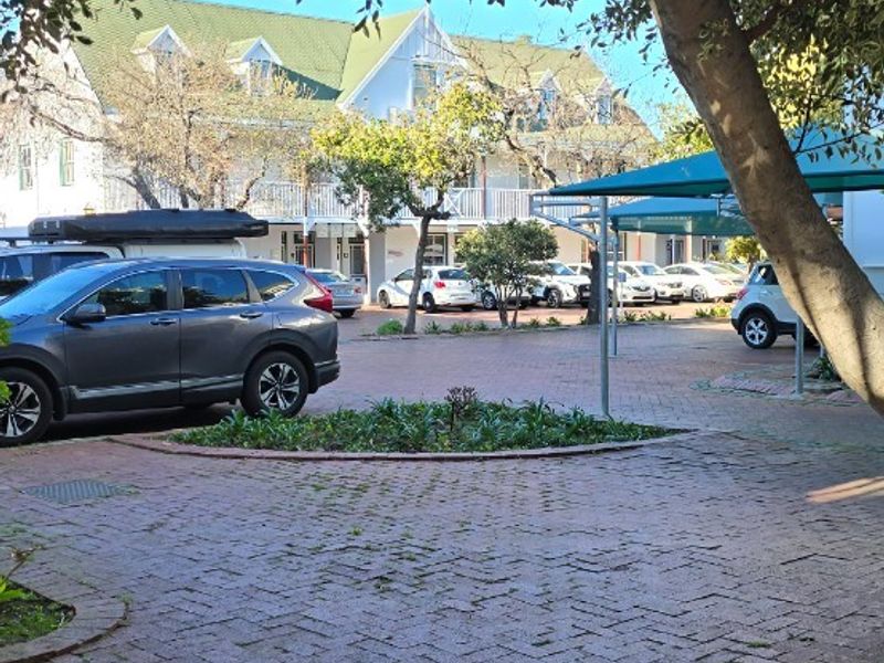Exterior view of the property frontage featuring brick paved driveway, covered parking bays, and established trees.