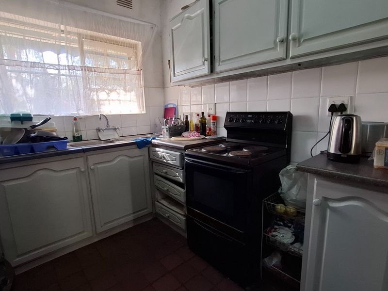 A compact kitchen featuring dated cabinetry, tiled backsplash, laminate countertops, and a freestanding electric stove, offering potential for modernization.