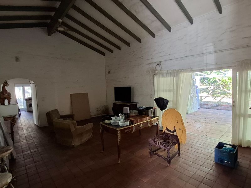 Spacious living area featuring exposed timber ceiling beams, terracotta floor tiles, and direct access to an outdoor patio through sliding glass doors.