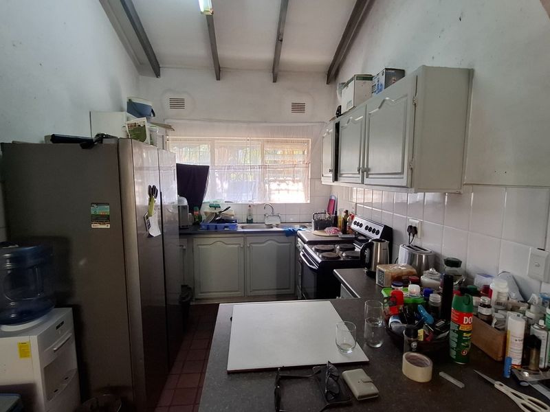A functional galley-style kitchen featuring built-in cabinetry, a tiled backsplash, and exposed ceiling beams, offering potential for a modern renovation.