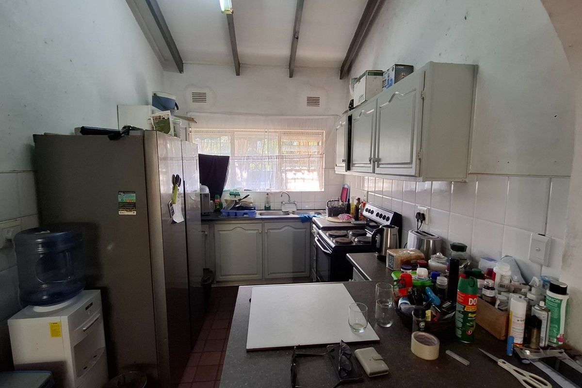 A functional galley-style kitchen featuring built-in cabinetry, a tiled backsplash, and exposed ceiling beams, offering potential for a modern renovation.