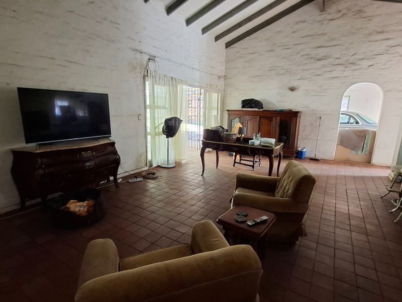 Spacious living area featuring high vaulted ceilings with exposed timber beams, terracotta tile flooring, and textured masonry walls with an arched transition to the kitchen.