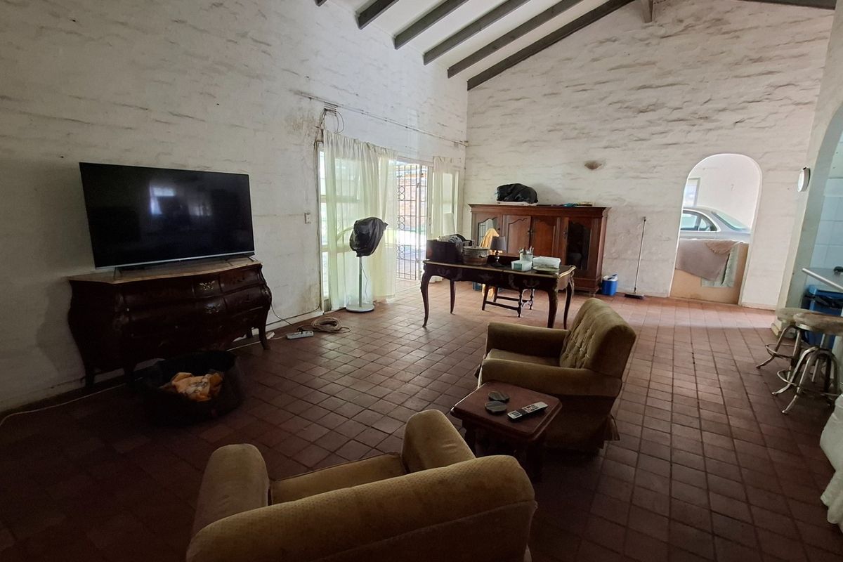 Spacious living area featuring high vaulted ceilings with exposed timber beams, terracotta tile flooring, and textured masonry walls with an arched transition to the kitchen.