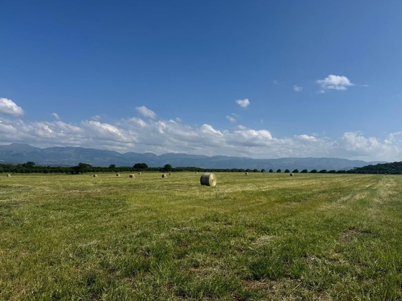 A wide-angle view of a sprawling farm pasture with hay bales and a scenic mountain range in the background.