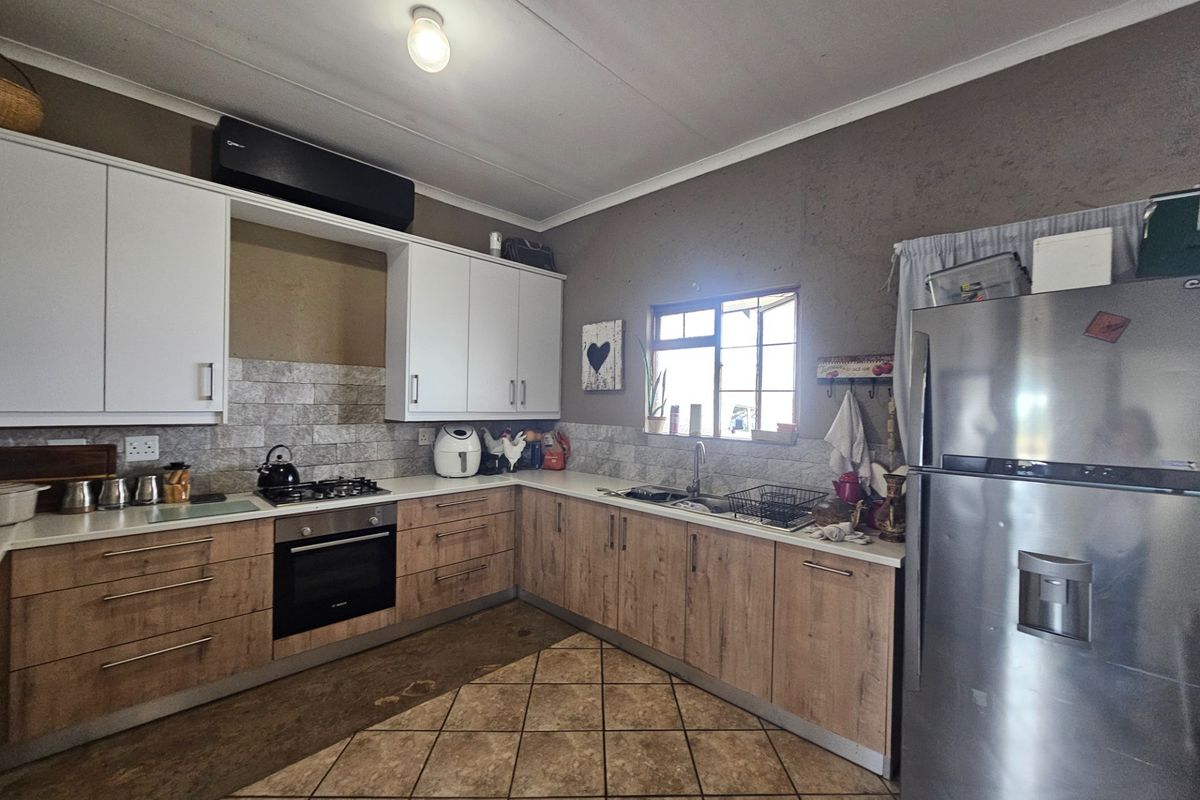 A functional kitchen featuring wood-look lower cabinetry, white upper cabinets, a gas hob, built-in oven, and tiled backsplash with a stainless steel sink.
