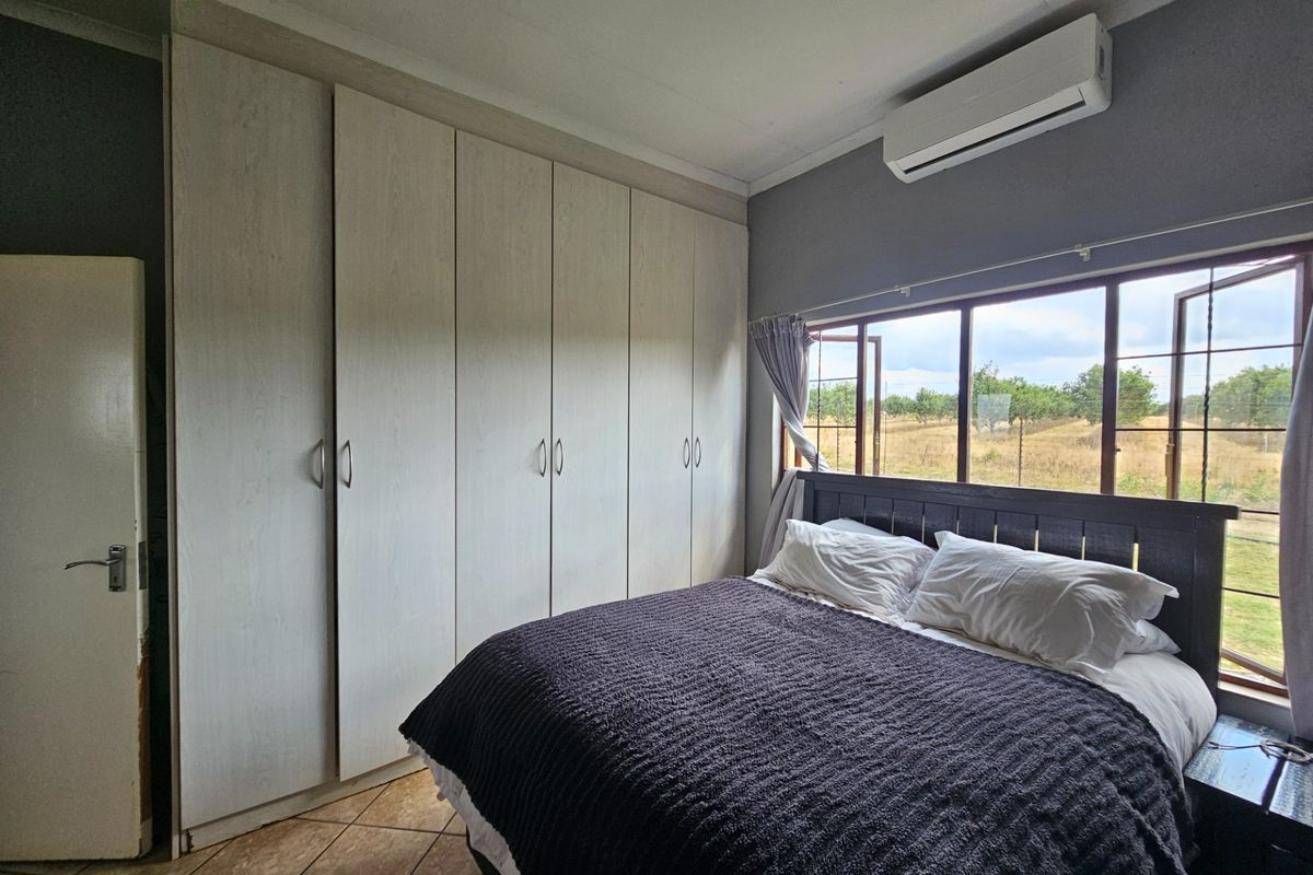A bedroom featuring built-in cupboards, tiled flooring, and a wall-mounted air conditioning unit, with views overlooking the surrounding farm landscape.