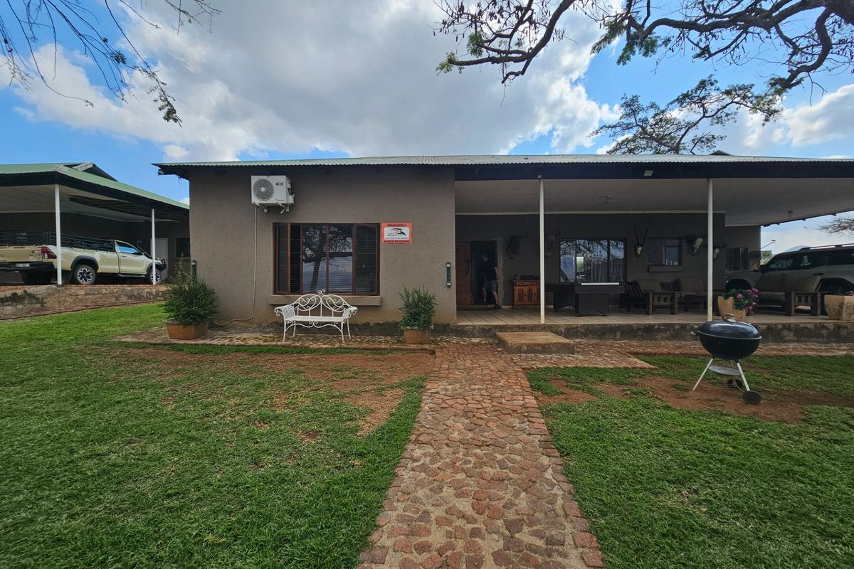 A rear view of the farm house featuring a covered patio, stone pathway, and well-maintained lawn area.