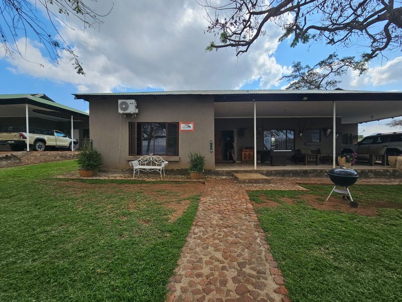 A rear view of the farm house featuring a covered patio, stone pathway, and well-maintained lawn area.