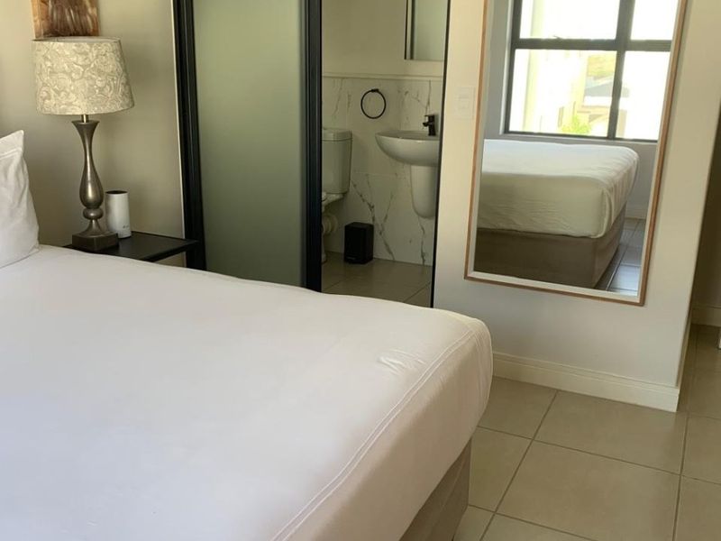A well-maintained bedroom featuring tiled flooring and an integrated en-suite bathroom with a pedestal basin and toilet.