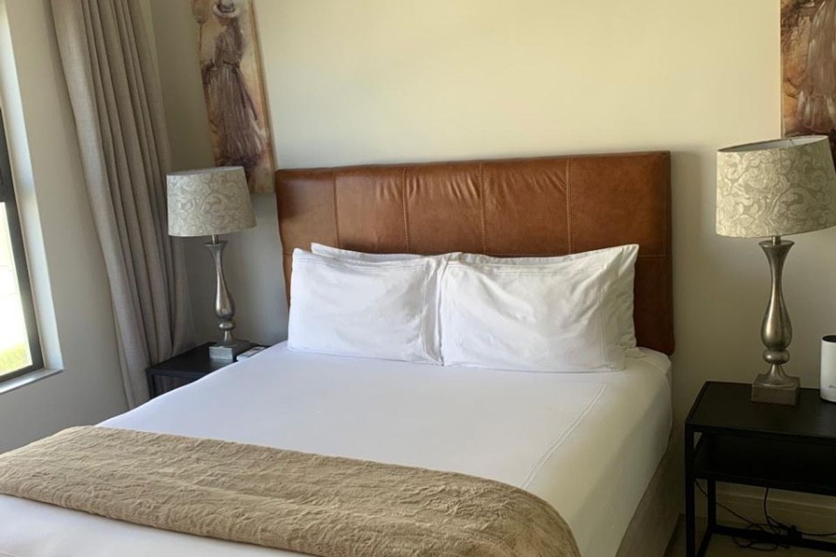 A well-maintained bedroom featuring neutral wall tones, tiled flooring, and large windows with installed curtain tracks.