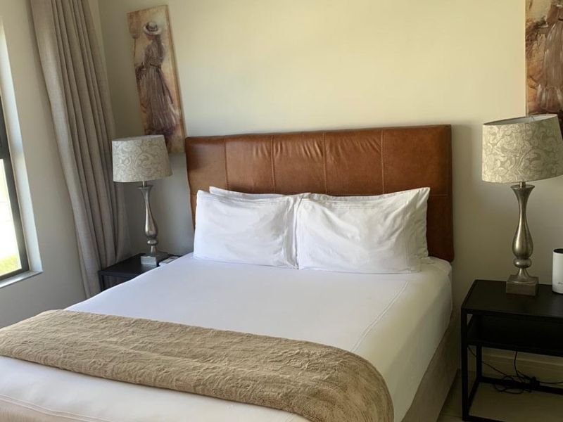 A well-maintained bedroom featuring neutral wall tones, tiled flooring, and large windows with installed curtain tracks.