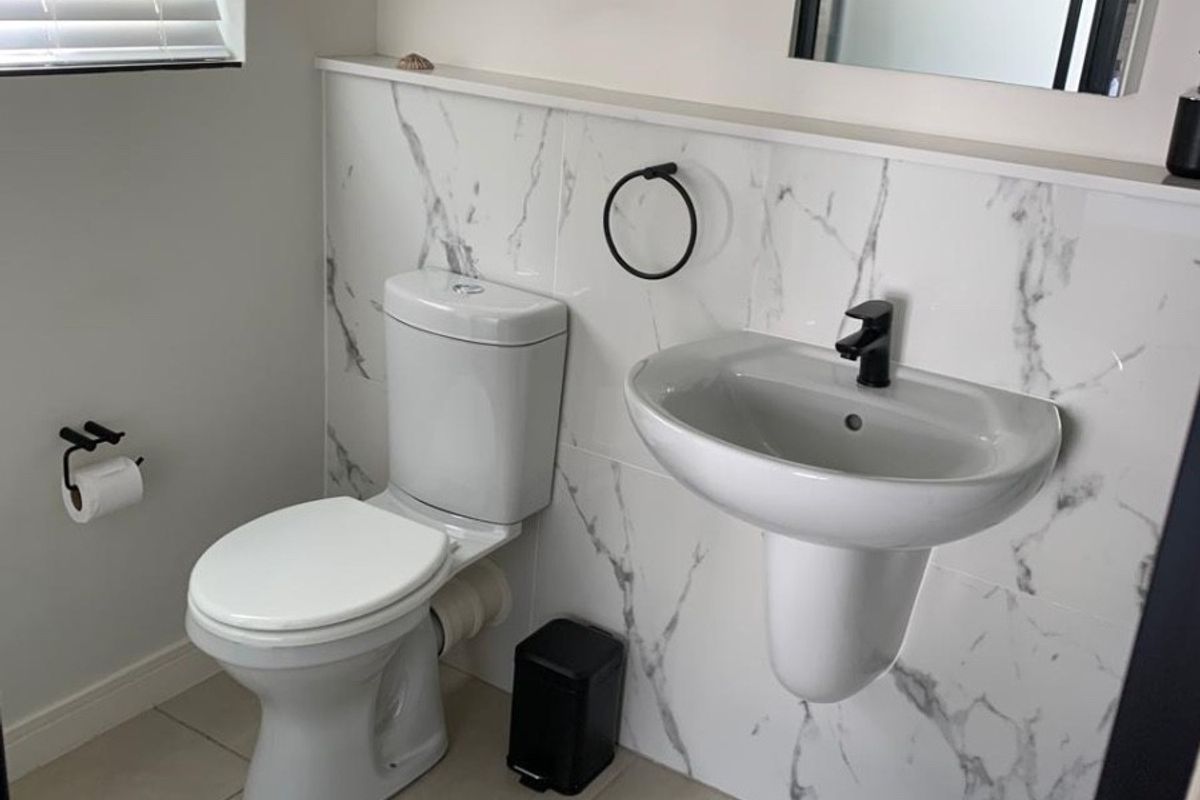 A modern bathroom featuring a wall-mounted basin, toilet, marble-look tiled splashback, and contemporary black fixtures.