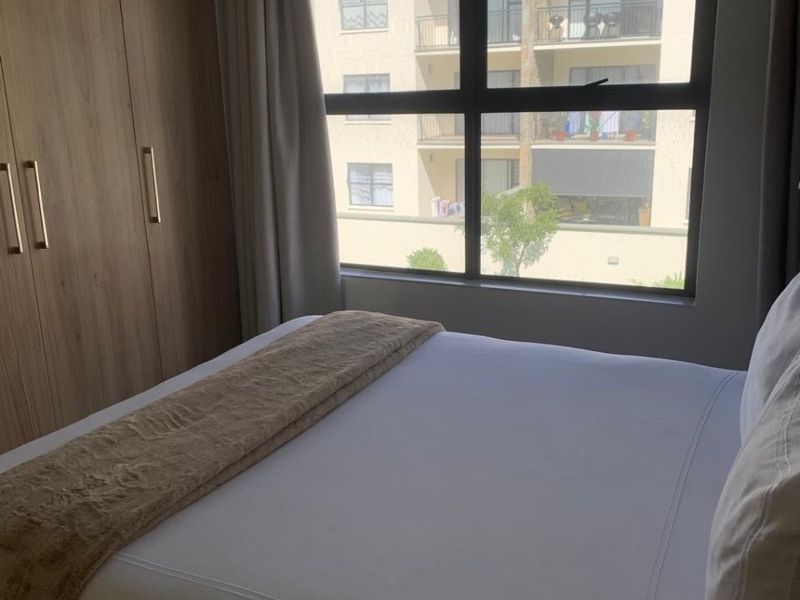 A well-maintained bedroom featuring a built-in wardrobe and a large window with views of the surrounding apartment complex.