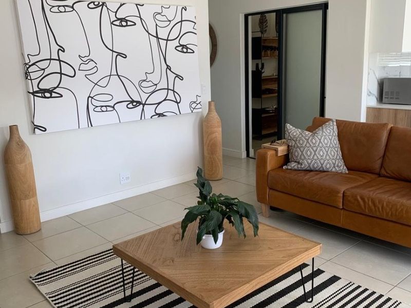 Modern open-plan living area featuring neutral tiled flooring and a seamless transition to the kitchen and adjacent room through a sliding glass door.