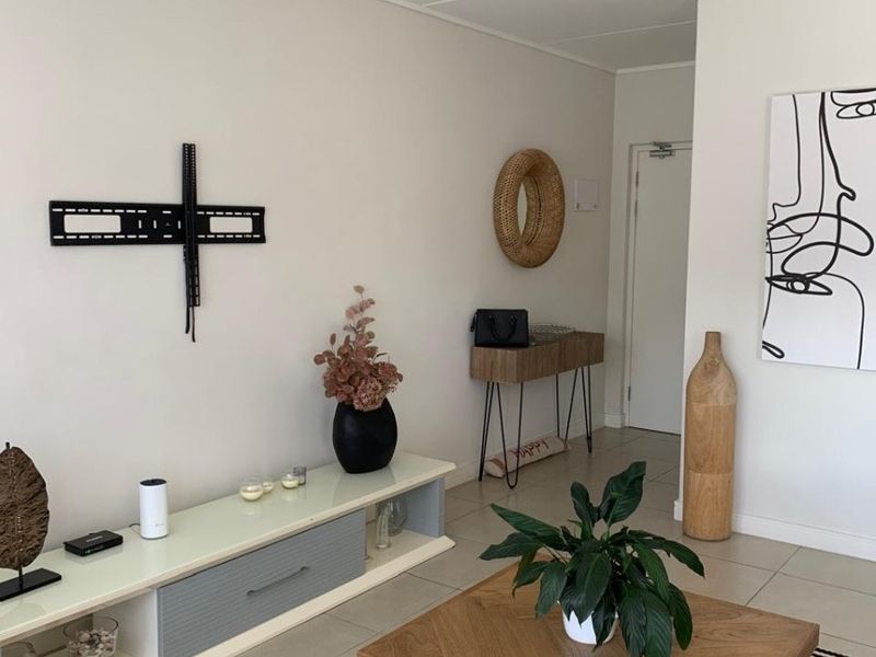 A bright and neutral living room featuring tiled flooring and a wall-mounted TV bracket, offering a clean and versatile space.