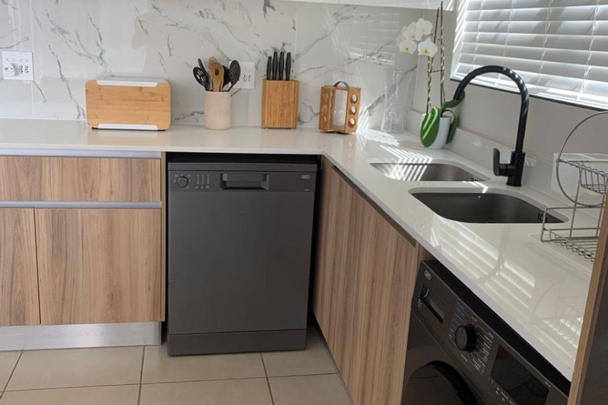 Modern kitchen featuring marble-look splashback, quartz countertops, integrated dishwasher, built-in washing machine, and sleek wood-veneer cabinetry with contemporary black fixtures.