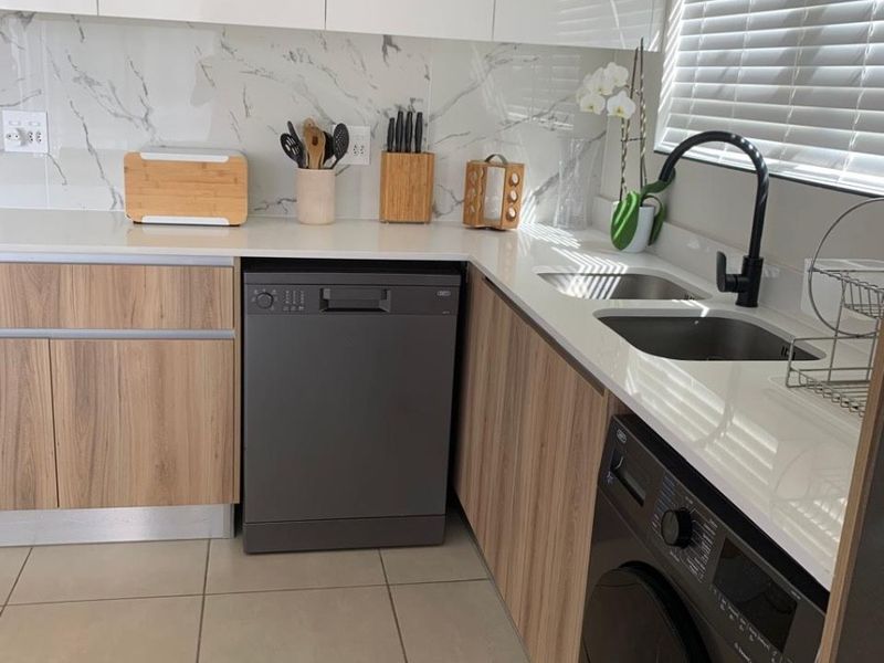 Modern kitchen featuring marble-look splashback, quartz countertops, integrated dishwasher, built-in washing machine, and sleek wood-veneer cabinetry with contemporary black fixtures.
