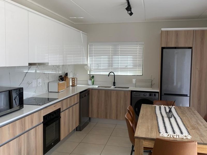 Modern open-plan kitchen featuring sleek white and wood-grain cabinetry, marble-look splashback, integrated appliances, and tiled flooring, seamlessly flowing into the dining area.