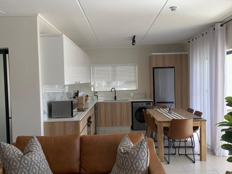 Modern open-plan living and kitchen area featuring contemporary cabinetry, integrated appliances, and neutral tiled flooring, creating a bright and functional living space.