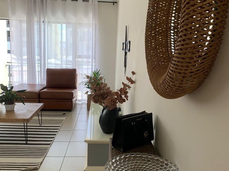 A bright living room featuring neutral tiled flooring, modern track lighting, and a large sliding glass door providing access to the balcony.