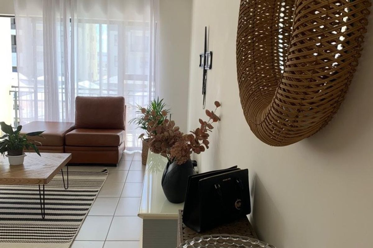 A bright living room featuring neutral tiled flooring, modern track lighting, and a large sliding glass door providing access to the balcony.
