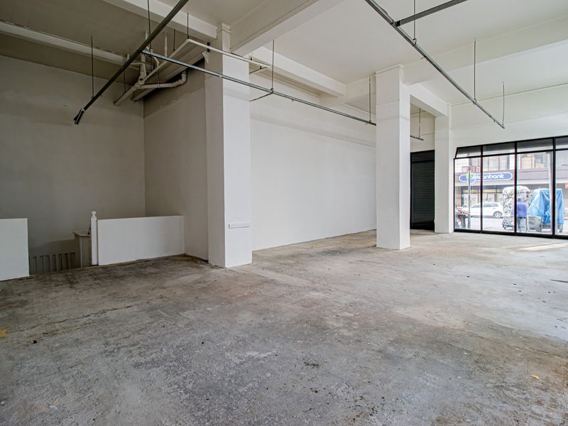 A spacious, empty commercial open-plan unit featuring exposed ceiling infrastructure, concrete flooring, and large glass storefront windows providing street visibility.