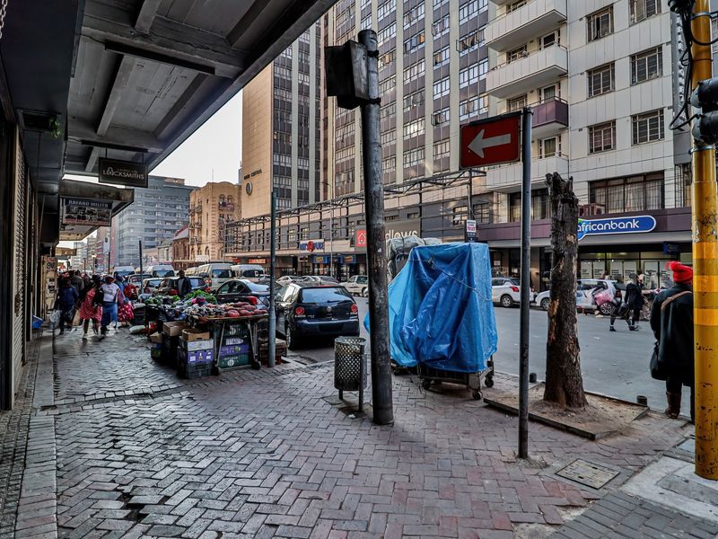 A street-level view of a busy urban commercial area featuring paved sidewalks, traffic infrastructure, and surrounding multi-story commercial buildings.