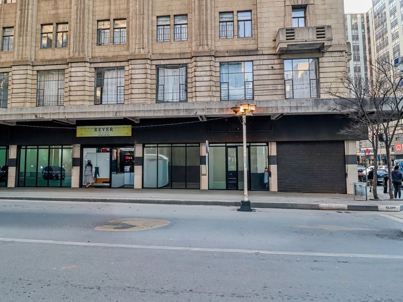 Street-level view of a commercial building facade featuring large display windows and a secure metal roller shutter door in an urban setting.