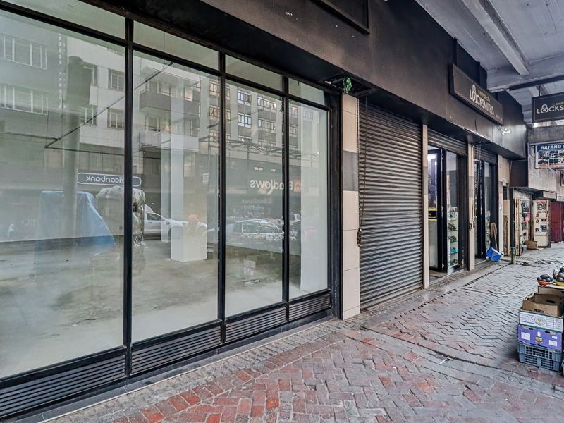 Commercial storefront featuring large glass display windows and a metal security roller shutter, located on a paved street-level sidewalk.