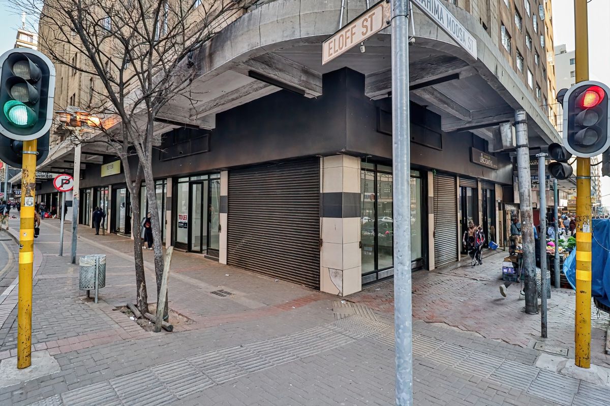 Corner commercial retail space featuring large display windows and metal roller shutters, located at a busy street intersection.