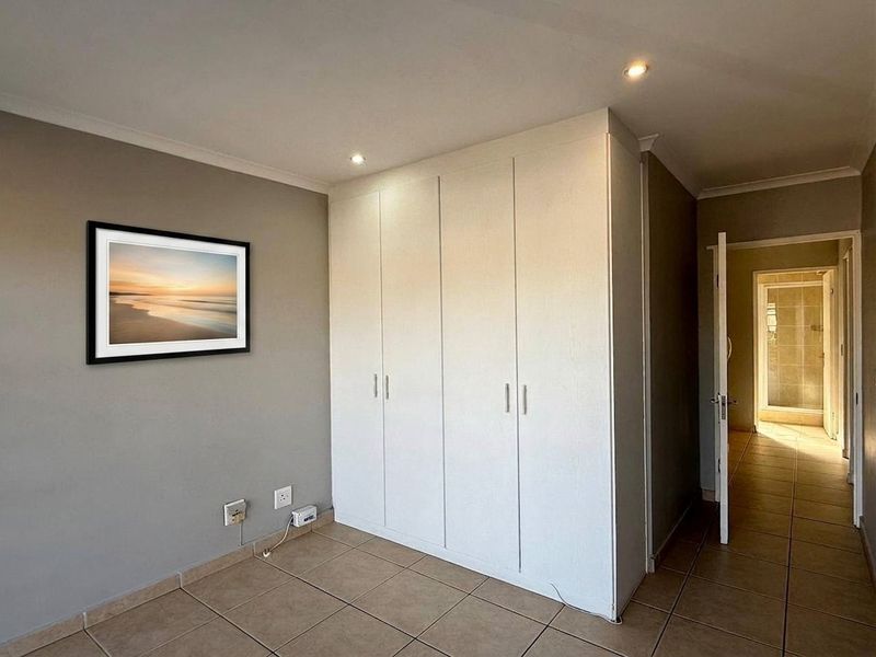 A clean, empty bedroom featuring neutral grey walls, tiled flooring, and a large built-in wardrobe with integrated storage.