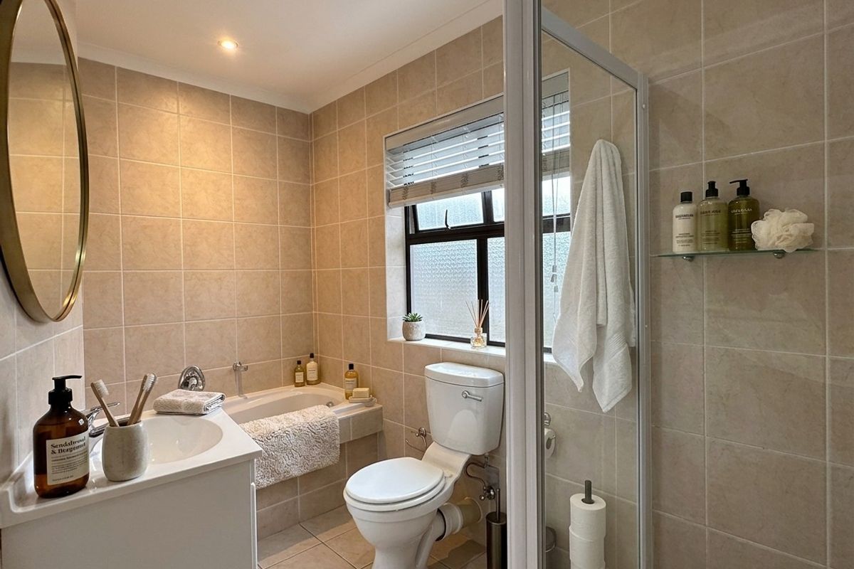 A well-maintained bathroom featuring a built-in bathtub, separate shower enclosure, vanity basin, and neutral floor-to-ceiling tiling.