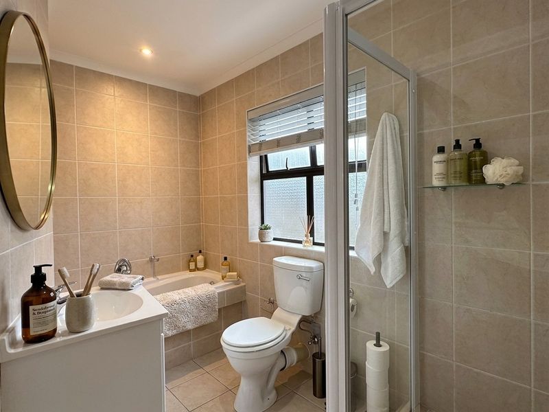 A well-maintained bathroom featuring a built-in bathtub, separate shower enclosure, vanity basin, and neutral floor-to-ceiling tiling.