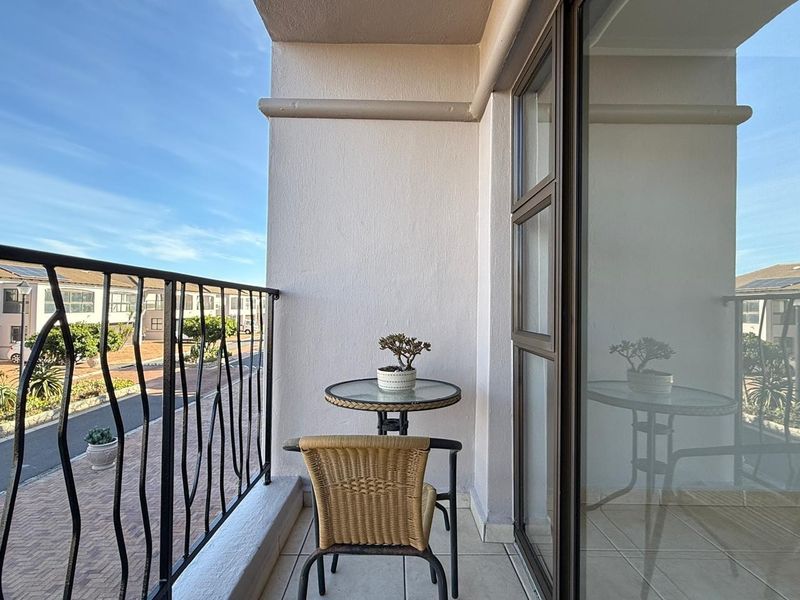 A private balcony featuring tiled flooring, a metal balustrade, and a sliding glass door providing access to the interior living space.