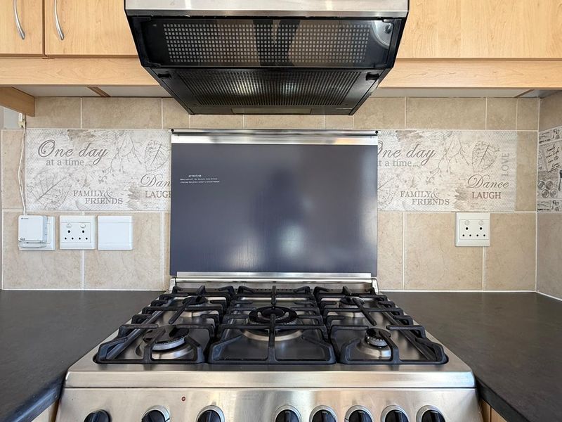 A clean kitchen cooking area featuring a stainless steel gas hob, integrated extractor fan, and decorative tiled backsplash with ample electrical points.