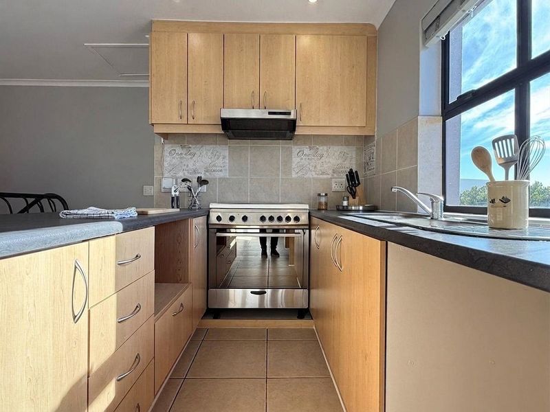 A functional kitchen featuring light wood cabinetry, laminate countertops, a tiled backsplash, and a stainless steel oven with an integrated extractor fan.