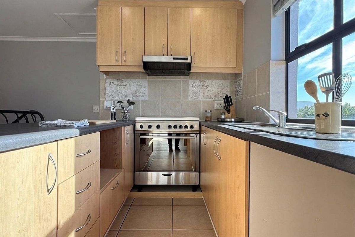 A functional kitchen featuring light wood cabinetry, laminate countertops, a tiled backsplash, and a stainless steel oven with an integrated extractor fan.