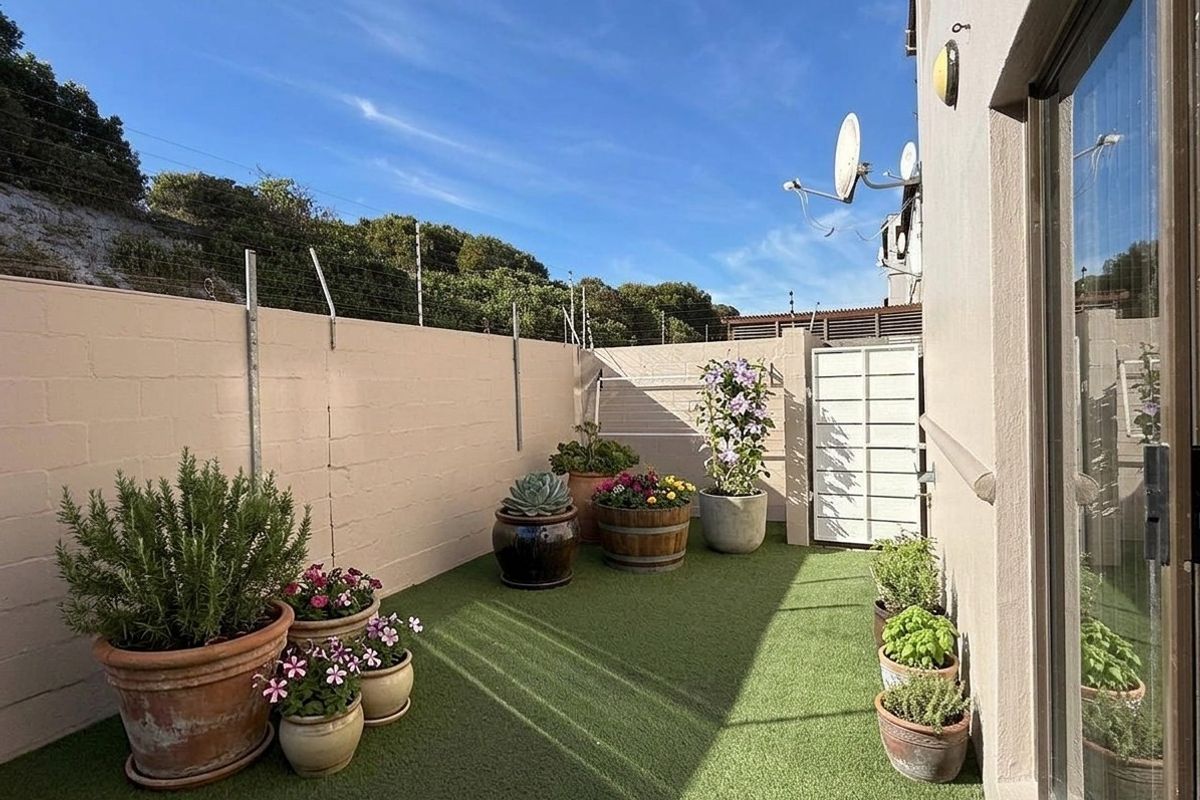 A private rear courtyard featuring artificial grass, secure boundary walls with electric fencing, and direct access to the home via a sliding door.