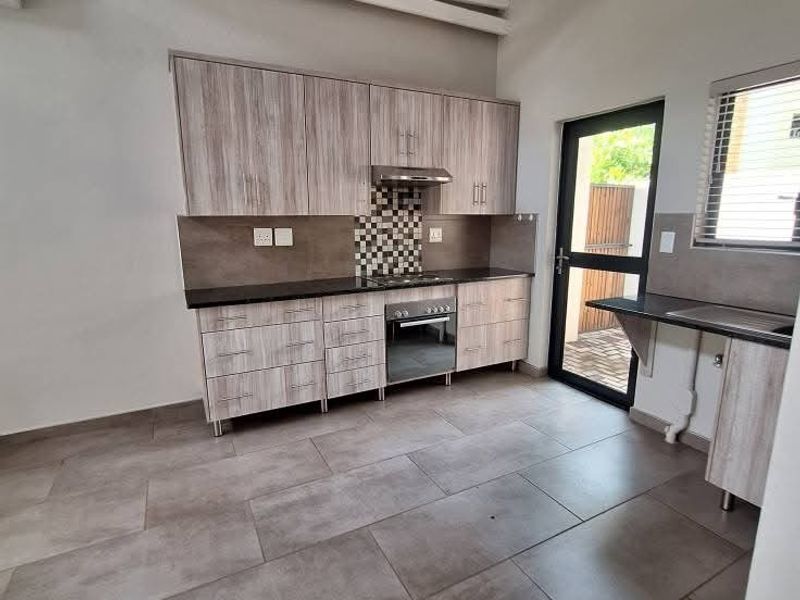 Modern kitchen featuring light wood-grain cabinetry, built-in oven and hob, tiled flooring, and high ceilings with exposed white trusses.