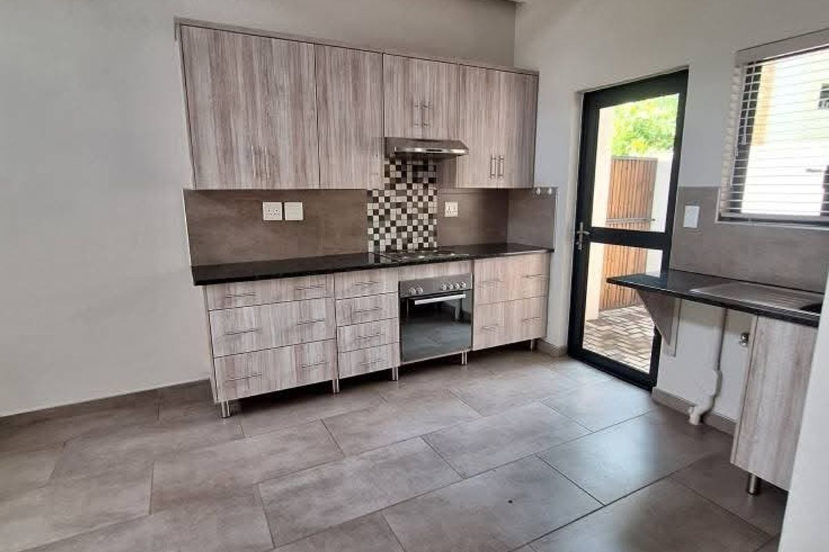 Modern kitchen featuring light wood-grain cabinetry, built-in oven and hob, tiled flooring, and high ceilings with exposed white trusses.