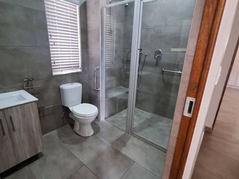 Modern bathroom featuring large format grey wall and floor tiles, a glass-enclosed walk-in shower, a vanity cabinet with basin, and a toilet.