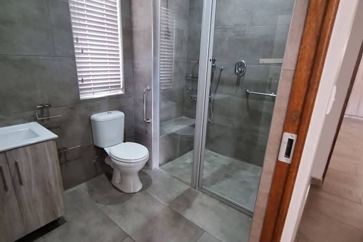 Modern bathroom featuring large format grey wall and floor tiles, a glass-enclosed walk-in shower, a vanity cabinet with basin, and a toilet.