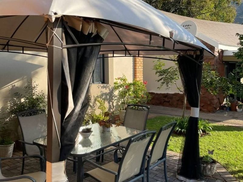 A paved outdoor patio area featuring a gazebo structure, providing a functional space for outdoor dining and relaxation in the garden.
