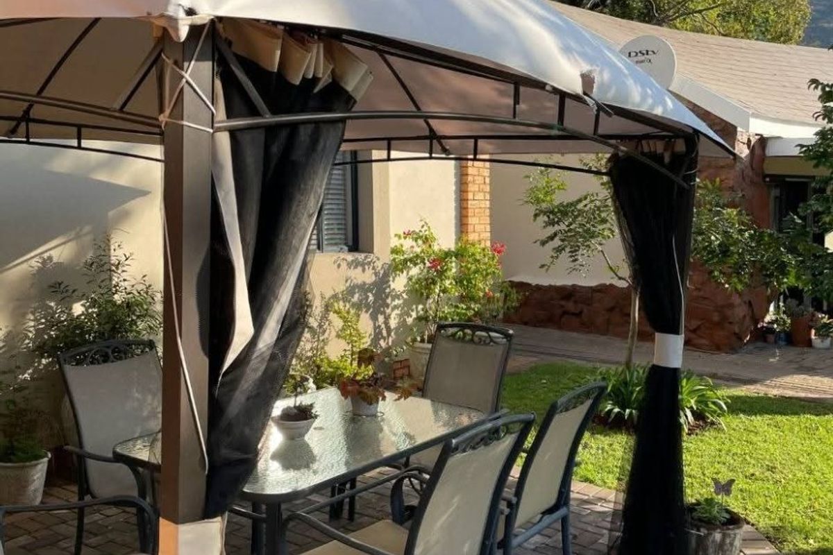 A paved outdoor patio area featuring a gazebo structure, providing a functional space for outdoor dining and relaxation in the garden.