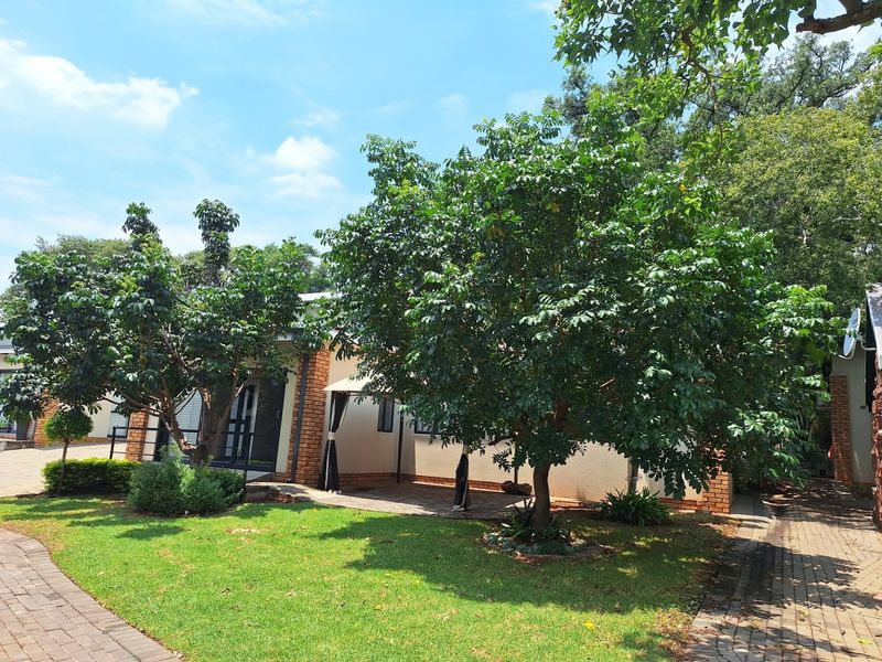 A well-maintained rear exterior view featuring a paved walkway, landscaped garden, and a covered patio area adjacent to the brick-accented building.