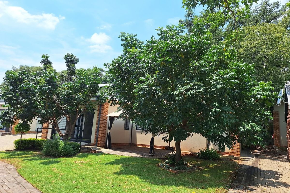 A well-maintained rear exterior view featuring a paved walkway, landscaped garden, and a covered patio area adjacent to the brick-accented building.