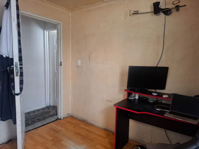 A small bedroom featuring laminate flooring and wall-mounted lighting, currently requiring cosmetic updates to the wall finishes.