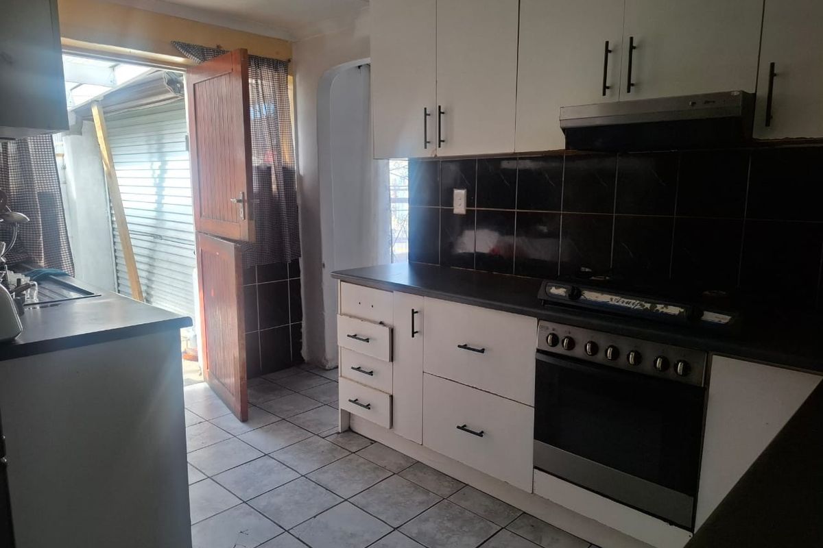 A functional kitchen featuring white cabinetry, tiled backsplash, and built-in cooking appliances, with direct access to an outdoor area.