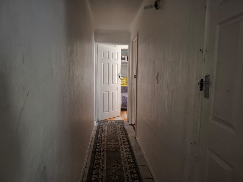 A narrow interior hallway featuring tiled flooring and multiple panel doors, showing signs of wear on the walls and door frames.